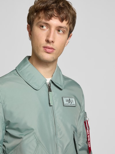 Męski model nosi bomberka Regular Fit Bomberjacke mit Logo-Patch od Alpha Industries w kolorze jasnoniebieskim, naszywka z logo, wykładany kołnierz, nakładane kieszenie, zamek błyskawiczny, elastyczne wykończenia, szerokość ramion w rozmiarze M: 44 cm, szerokość klatki piersiowej w rozmiarze M: 56 cm, długość rękawów w rozmiarze M: 66 cm, długość tyłu w rozmiarze M: 66 cm, półzbliżenie przód