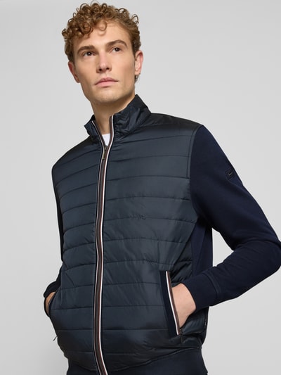 Männermodel trägt Regular Fit Jacke in Stepp-Optik Modell 'Selanik' von bugatti, Mieszanka bawełny, Stójka, wpuszczane kieszenie z zamkiem błyskawicznym, zamek błyskawiczny, elastyczne wykończenia, długość tyłu w rozmiarze M: 70 cm, długość rękawów w rozmiarze M: 69 cm, granatowe odcienie, prostokątne przeszycia, gładka tekstura, Nahaufnahme górnej części ciała.