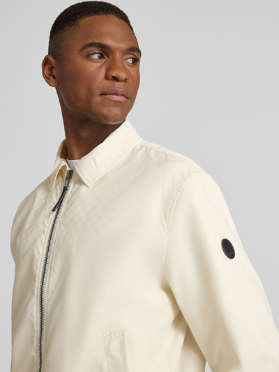 Männermodel trägt cremefarbene Jacke mit Reißverschluss Modell 'Salvador' von JOOP! Collection, Label-Detail, Nahaufnahme Oberkörper.