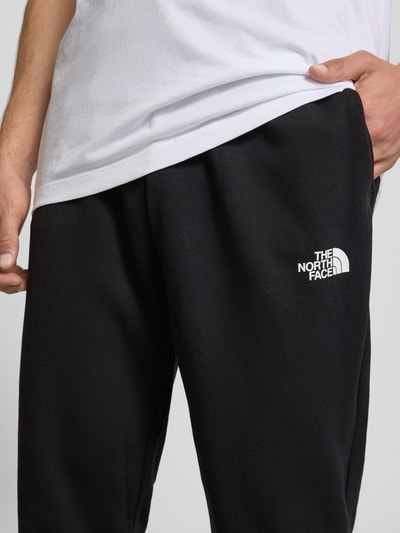 Männermodel trägt Sweatpants mit Logo-Print von The North Face, Baumwoll-Mix, Slim-Fit, schwarze Farbe, Nahaufnahme Oberkörper.