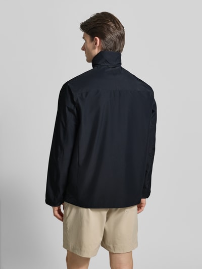 Męski model nosi Regular Fit Jacke mit Logo-Print Modell 'Quest' od PEAK PERFORMANCE, czarna, krój regular fit, widok całej sylwetki z tyłu, długość tyłu w rozmiarze M 74 cm, szerokość ramion w rozmiarze M 45 cm, szerokość klatki piersiowej w rozmiarze M 55 cm, długość rękawa w rozmiarze M 65 cm.
