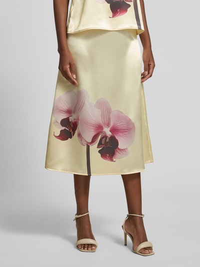 Frauenmodel trägt Midirock aus Satin mit Motiv-Print und elastischem Bund von YAS in Creme mit rosa Blüten, A-Linie, Nahaufnahme Unterkörper. Bundweite 36 cm, Gesamtlänge 82 cm, Größe 36.