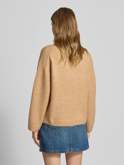 Kobiece modelka ma na sobie Sweter z dzianiny z dodatkiem wełny od Gina Tricot, luźny krój, prążkowane wykończenia, okrągły dekolt, mieszanka materiałów, długość tyłu 59 cm, długość rękawa 66 cm, kolor beżowy, denimowa spódnica, widok całej sylwetki z tyłu.