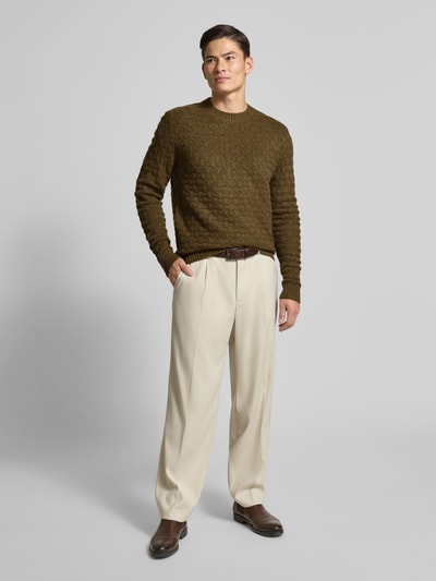 Männermodel trägt Regular Fit Strickpullover mit Woll-Anteil Modell 'BLASIMON' von Jack & Jones Premium in Oliv mit Strukturmuster, Gerippte-Abschlüsse, Rundhalsausschnitt, Material-Mix, Kombi mit heller Hose, Ganzkörperansicht von vorne.