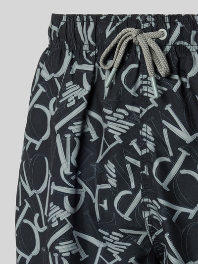 Männermodel trägt Regular Fit Shorts mit Allover-Logo-Print von Emporio Armani, schwarzer Stoff mit grauem Muster, elastischer Bund, Tunnelzug, Nahaufnahme Oberkörper.