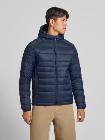 Męski model nosi Regular Fit kurtkę w z efektem pikowania Model 'Kingsley' od JACK & JONES, granatowy kolor, stójka, zamek błyskawiczny, wpuszczane kieszenie, Długość tyłu w rozmiarze M: 72 cm, Szerokość ramion w rozmiarze M: 48 cm, Szerokość klatki piersiowej w rozmiarze M: 51 cm, Długość rękawów w rozmiarze M: 68 cm, zdjęcie w całej sylwetce z przodu.