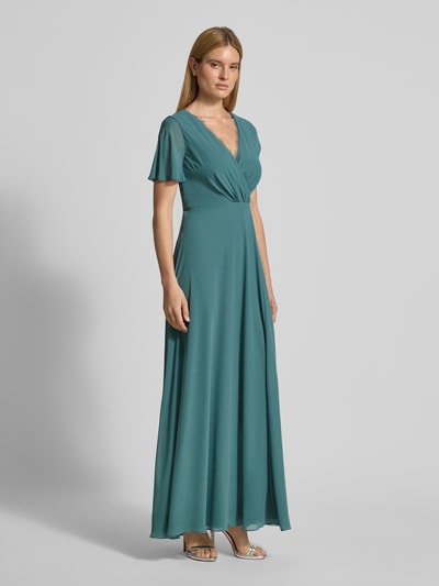 Frauenmodel trägt Damen Abendkleid mit Spitzenbesatz von Christian Berg Cocktail in Taillierter Passform, V-Ausschnitt, Wickel-Optik, Kurzarm, semitransparent mit Raffungen, fließende Textur, smaragdgrün, Ganzkörperansicht von vorne.