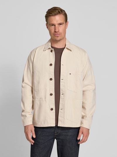 Męski model nosi Regular Fit Hemdjacke aus reiner Baumwolle von Tommy Hilfiger, jednokolorowy, wykładany kołnierz, listwa guzikowa, wyhaftowane logo, długi rękaw z mankietami, nakładana kieszeń na piersi, wpuszczane kieszenie, wykończenie materiału: rigid denim, bawełna, Ganzkörperansicht von vorne.