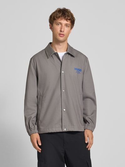 Männermodel trägt Relaxed Fit Blouson aus reiner Baumwolle Modell 'Biyo2631' von HUGO, grauer Stoff, blaue Details, Ganzkörperansicht von vorne, Herren Bomberjacke / Blouson von HUGO Blue.