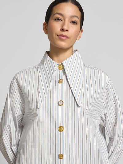 Modelka kobieca nosi Oversized Hemdbluse aus reiner Baumwolle Modell 'JOMATO' od Essentiel Antwerp, biała z cienkimi paskami, kołnierz koszulowy, długi rękaw, czysta bawełna, detal guzików, ujęcie z przodu, zbliżenie na górę ciała.