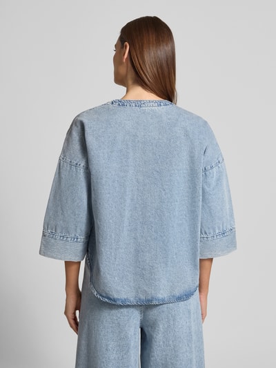 Vrouwenmodel draagt Loose fit jeansblouse uit katoen- en viscosemix Model 'VALERIA' van Vero Moda in denimlook, lichtblauw, 3/4-mouwen, rompzoom afgerond, knoopsluiting, schouderpartijen verlaagd. Ganzkörperansicht Rückansicht.