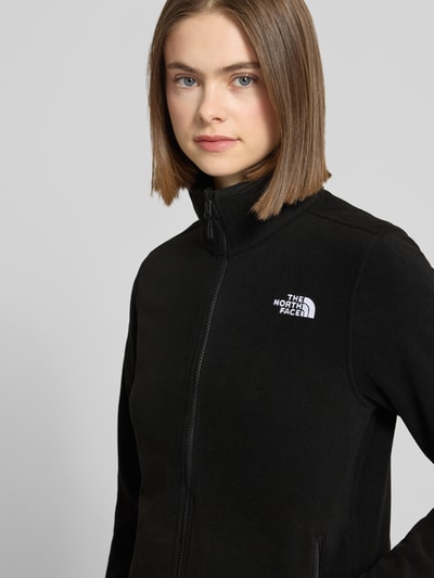 Frauenmodel trägt schwarze Fleecejacke mit Stehkragen, Label-Stitching, Reißverschlusstaschen, Slim Fit, Modell 'GLACIER' von The North Face, Nahaufnahme Oberkörper. Rückenlänge bei Größe S: 62 cm, Schulterbreite bei Größe S: 39 cm, Brustweite bei Größe S: 47 cm, Ärmellänge bei Größe S: 62 cm.