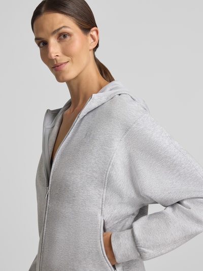 Modelka kobieca nosi szarą bluzę rozpinaną 'Regular Fit Sweatjacke mit Baumwoll-Anteil' od Under Armour, zbliżenie na górną część ciała.
