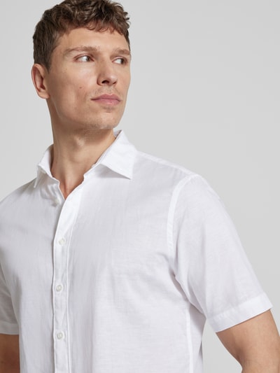 Męski model nosi Slim Fit Freizeithemd aus Leinen-Mix von Jake*s, mieszanka bawełny i lnu, krój slim fit, kołnierzyk typu kent, krótki rękaw, listwa guzikowa, długość tyłu w rozmiarze M: 73 cm, szerokość ramion w rozmiarze M: 47 cm, długość rękawów w rozmiarze M: 26 cm, biała, gładka tekstura, z przodu, zbliżenie na górną część ciała