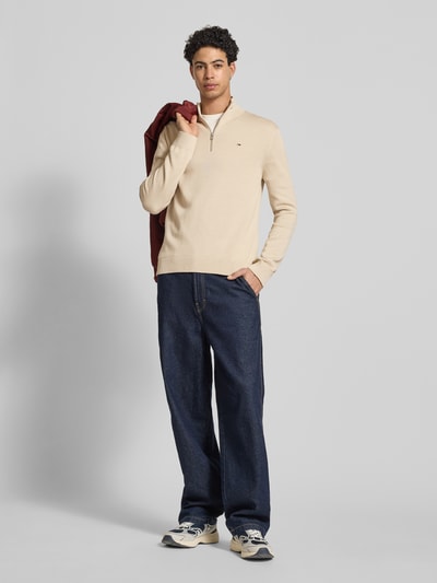 Männermodel trägt Slim Fit Troyer aus reiner Baumwolle von Tommy Jeans in Optik: Unifarben, Feinstrick, Logo-Detail, Ganzkörperansicht von vorne.