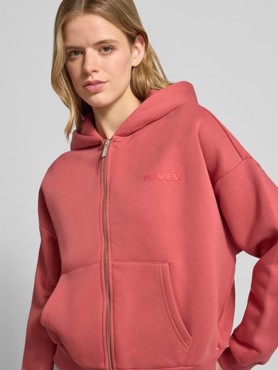 Frauenmodel trägt Relaxed Fit Sweatjacke mit Kapuze und Logo-Print von REVIEW aus Baumwoll-Mix, Reißverschluss, Känguru-Tasche, Nahaufnahme Oberkörper.