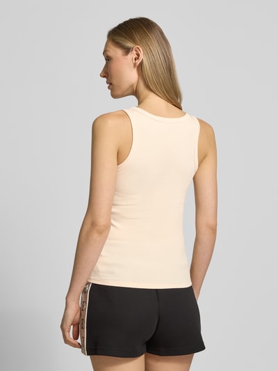 Frauenmodel trägt Slim Fit Top aus Viskose-Mix Modell 'Colette' von Guess Activewear in Beige mit Logo-Applikation, Ganzkörperansicht Rückansicht.