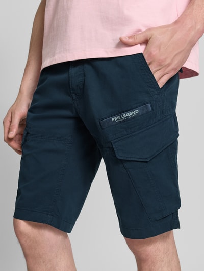 Männermodel trägt Tapered Fit Cargo Bermudas mit Pattentaschen Modell 'Nordrop' von PME Legend, dunkelblauer Baumwoll-Mix mit Stretch, Label-Patch, Nahaufnahme Oberkörper und Shorts, seitliche Eingrifftaschen und Gesäßleistentaschen sichtbar.