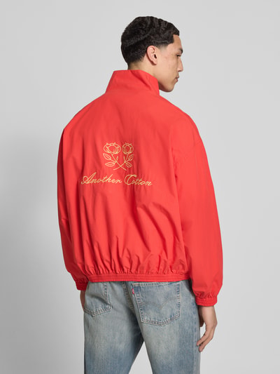 Męski model nosi Segeljacke mit Stehkragen und Logo-Stitching von ANOTHER COTTON LAB, czerwona bawełna, prosty krój, zamek błyskawiczny dwustronny, wyhaftowane logo, elastyczne wykończenia, długość tyłu w rozmiarze M: 63 cm, szerokość ramion w rozmiarze M: 60 cm, szerokość w klatce piersiowej w rozmiarze M: 63 cm, długość rękawów w rozmiarze M: 55 cm, widok całej sylwetki z tyłu