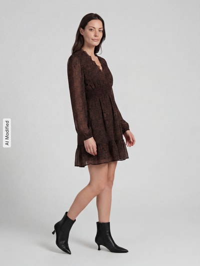Frauenmodel trägt Minikleid mit elastischem Taillenband und V-Ausschnitt von Apricot, Chiffon, taillierter Schnitt, Allover-Look, Rüschen, Schwarz-Braun-Töne, leichte Textur, Ganzkörperansicht von vorne.