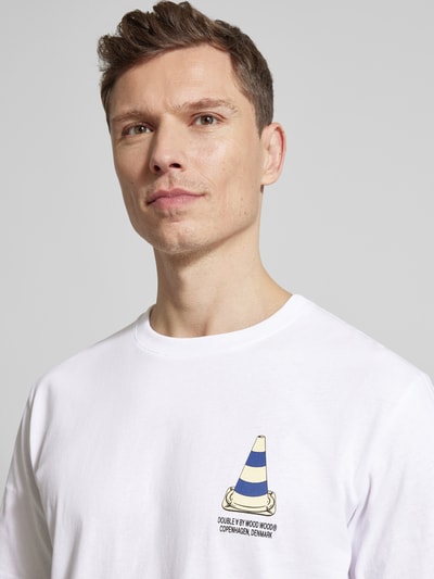 Mężczyzna nosi T-Shirt mit rückseitigem Motiv- und Logo-Print von Wood Wood z bawełny, krój regular fit, biały, detal z przodu, zbliżenie na górną część ciała.