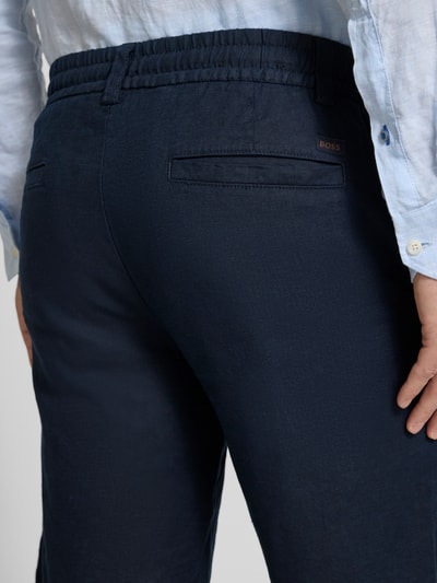Männermodel trägt Tapered Chinoshorts aus Leinen-Mix Modell 'DS_3S' von BOSS Orange in Dunkelblau mit elastischem Bund, Detailaufnahme Rückansicht.