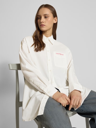 Frauenmodel trägt Oversized Hemdbluse aus Baumwoll-Mix von Tommy Jeans in Optik: Unifarben mit Hemdkragen, Label-Schriftzug, Rückenpasse, einreihige Knopfleiste, Langarm, Manschette, leicht abgerundetem Rumpfabschluss und Materialverarbeitung: Popeline; Ganzkörperansicht von vorne.