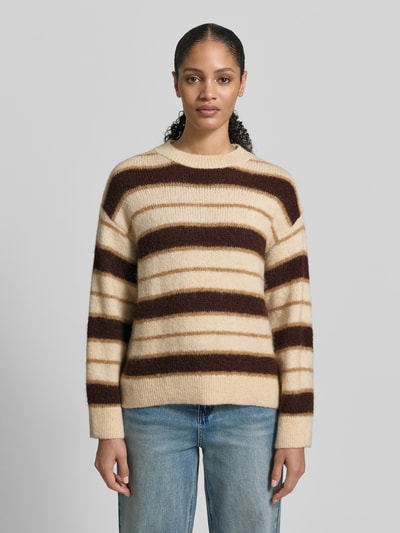 Frauenmodel trägt Strickpullover mit gerippten Abschlüssen von Mango, Material-Mix mit Baumwoll-Anteil, lockerer Schnitt, Beige-Braun gestreift, Rundhalsausschnitt, Ganzkörperansicht von vorne.