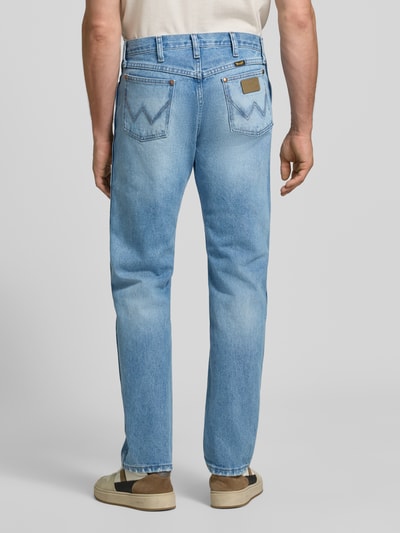 Männermodel trägt Bootcut Jeans aus reiner Baumwolle von Wrangler, denim w jasnoniebieskim kolorze, naszywka z logo, 5 kieszeni, szlufki, splot twill, całkowity widok od tyłu.