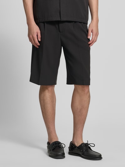Männermodel trägt Straight Fit Shorts mit Viskose-Anteil von Lindbergh in Schwarz mit Bundfalten, Gesäßtaschen, Haken-Reißverschluss, Nahaufnahme Unterkörper.