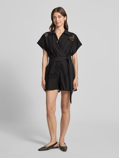 Frauenmodel trägt Jumpsuit in Wickel-Optik Modell 'TRACY' von SUNCOO PARIS aus Reine Baumwolle mit Lochstickerei, Relaxed-Fit, Bindegürtel, schwarze Farbe, Ganzkörperansicht von vorne.