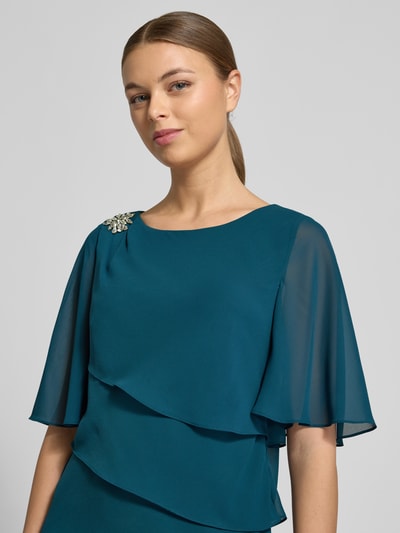 Frauenmodel trägt Relaxed Fit Kleid mit Ziersteinbesatz von Christian Berg Cocktail in Petrol, semitransparente Ärmel, Nahaufnahme Oberkörper.