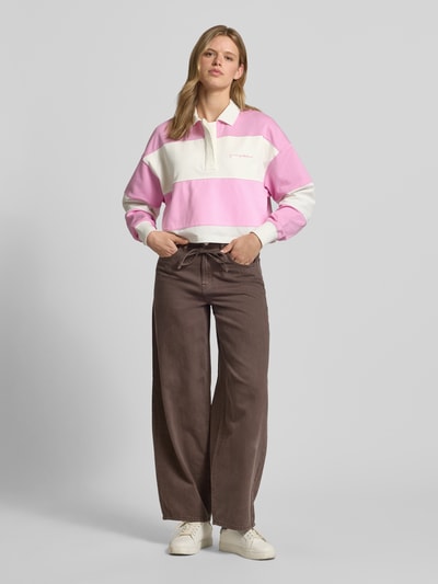 Frauenmodel trägt Relaxed Fit Sweatshirt aus reiner Baumwolle von Marc O'Polo Denim mit rosa-weißem Allover-Streifenmuster, Polokragen und geripptem Ärmelabschluss, kombiniert mit weiter Hose, Ganzkörperansicht von vorne.