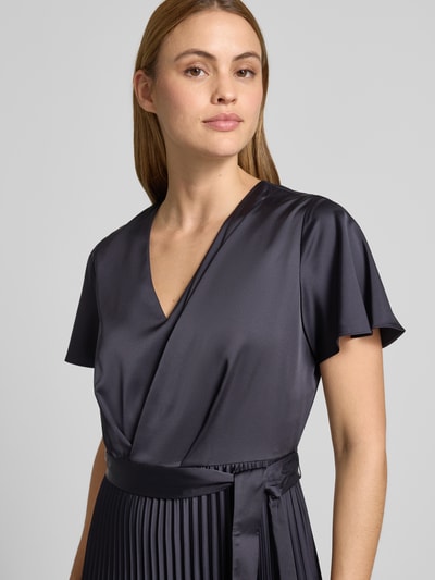 Frauenmodel trägt Midikleid aus Satin mit V-Ausschnitt von comma in Dunkelgrau, taillierte Passform, plissierte Optik, Stoffband, Nahaufnahme Oberkörper.