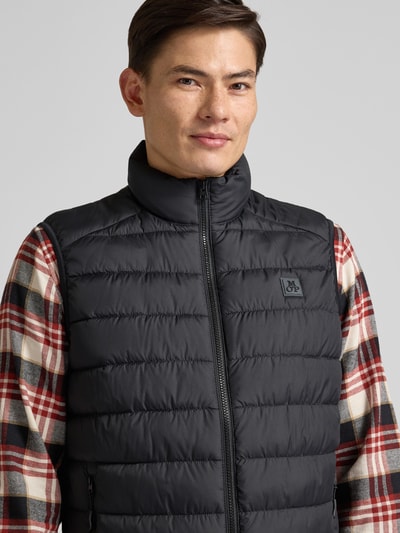 Männermodel trägt Steppweste mit Stehkragen von MARC O'POLO, Regular-Fit, Reißverschlusstaschen, Label-Detail, Nahaufnahme Oberkörper.