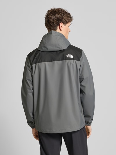 Mężczyznamodel nosi Regular Fit Jacke mit Logo-Print Modell 'Antora' von The North Face w odcieniach szarości z czarnymi detalami, matowa tekstura, kaptur z troczkiem, kieszenie boczne, elastyczne mankiety, długość pleców w rozmiarze M: 74 cm, szerokość ramion w rozmiarze M: 47 cm, szerokość klatki piersiowej w rozmiarze M: 58 cm, długość rękawa w rozmiarze M: 68 cm, widok całej sylwetki z tyłu