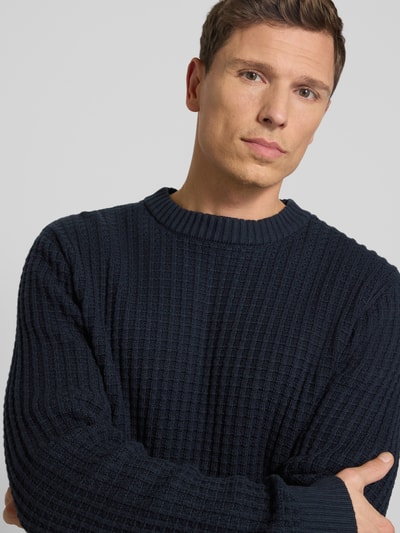 Männermodel trägt Regular Fit Strickpullover aus reiner Bio-Baumwolle Modell 'TOM' von SELECTED HOMME, structuur, donkerblauw. Nahaufnahme Oberkörper.