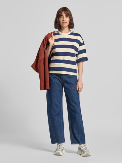 Frauenmodel trägt Oversized T-Shirt aus reiner Baumwolle von s.Oliver RED LABEL mit breiten Querstreifen in Blau und Creme, dazu Jeans und Sportschuhe, Ganzkörperansicht von vorne.