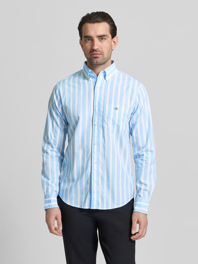 Männermodel trägt Slim Fit Freizeithemd mit Brusttasche von Gant, hellblau-weiß gestreift, Langarm, Button-Down-Kragen, Ganzkörperansicht von vorne.