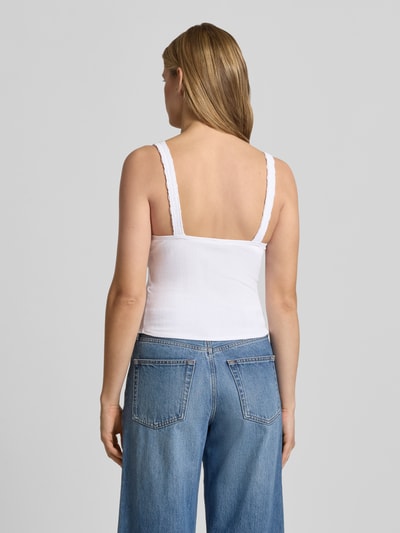Vrouwenmodel draagt 'Slim Fit Top mit Spitzenbesatz' van Guess Jeans in wit, elastische katoenmix met modal, rechte rug, kanten rand, sierstrik en mouwloos design, slim fit, V-hals, eenvoudig oppervlak, gecombineerd met blauwe denim, ruglengte bij maat S 26 cm, volledige lichaamsweergave achteraan.