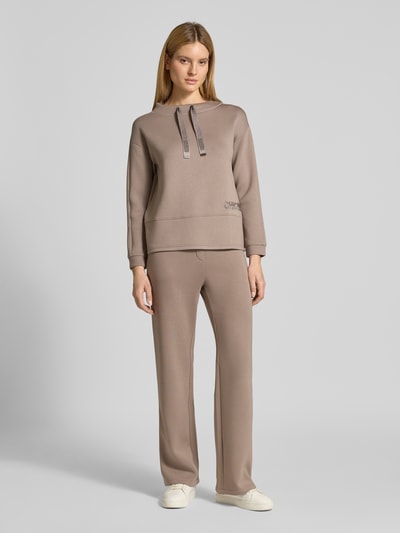 Frauenmodel trägt Stoffhose mit elastischem Bund von Betty Barclay, Viskose-Mix mit Stretch-Anteil und Label-Detail, lockerer Schnitt, französische Eingrifftaschen, Gesäßtaschen, Bundweite 106 cm bei Größe 36, Innenbeinlänge 78 cm bei Größe 36, sandfarbener Ton, glatte Textur, Ganzkörperansicht von vorne.