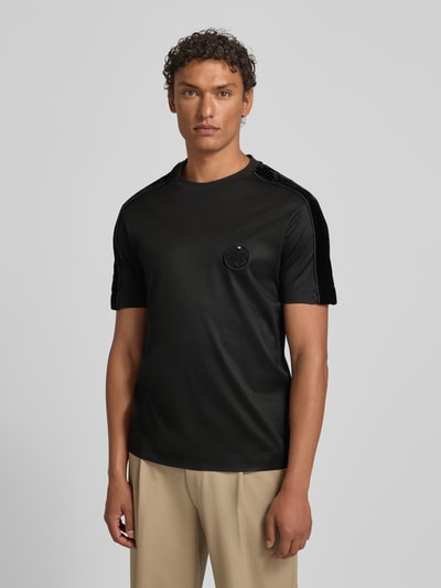 Männermodel trägt T-Shirt mit Label-Detail von Emporio Armani in Schwarz aus Lyocell-Baumwoll-Mix, Regular-Fit, gerippter Rundhalsausschnitt, Rückenlänge 70 cm bei Größe M, Ganzkörperansicht von vorne.