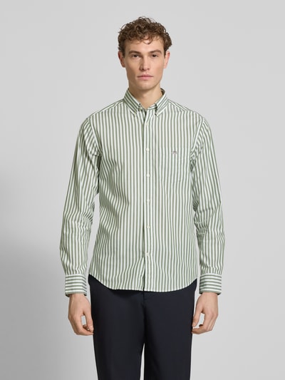 Męski model nosi Slim Fit Freizeithemd mit Brusttasche od Gant, zielono-białe paski, czysta bawełna, długi rękaw, guziki, logo, krój slim fit, kieszeń na piersi, zaokrąglony dół, długość pleców w rozmiarze M: 77 cm, szerokość w rozmiarze M: 46 cm, długość rękawa w rozmiarze M: 65 cm, widok całej sylwetki z przodu.