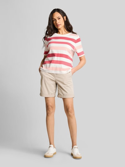Modelka kobieca nosi Relaxed Fit T-Shirt aus reiner Baumwolle od Tom Tailor w paski, wzór allover, okrągły dekolt, jersey, krótki rękaw, kremowo-różowe i czerwone kolory, widok całej sylwetki z przodu.