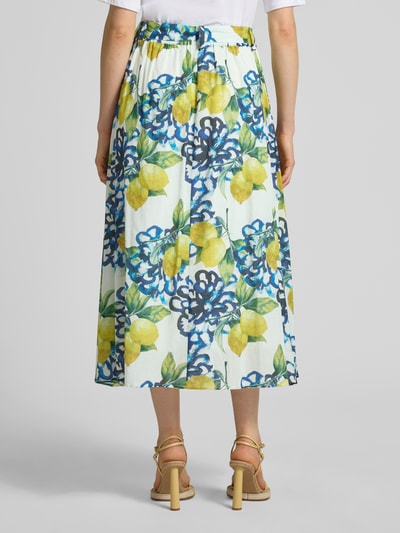 Frauenmodel trägt Regular Fit Midirock mit floralem Allover-Print von More & More, gelb-blau-grünes Muster, reine Baumwolle, Ganzkörperansicht Rückansicht.