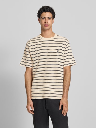 Männermodel trägt Strukturiertes T-Shirt mit Logostickerei auf der Brust von REVIEW, beige-schwarz, Reine Baumwolle, Gerader-Schnitt, Rundhalsausschnitt, Lochstickerei, Strukturmuster, Rückenlänge 70 cm, Ganzkörperansicht von vorne.