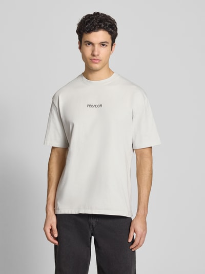 Männermodel trägt Oversized T-Shirt aus Baumwolle Modell 'Stavoren' von Pegador in hellem Beige mit Label-Detail, Halbarm, Rundhalsausschnitt, Oversized-Fit, Rückenlänge bei Größe M 70 cm, Ganzkörperansicht von vorne.