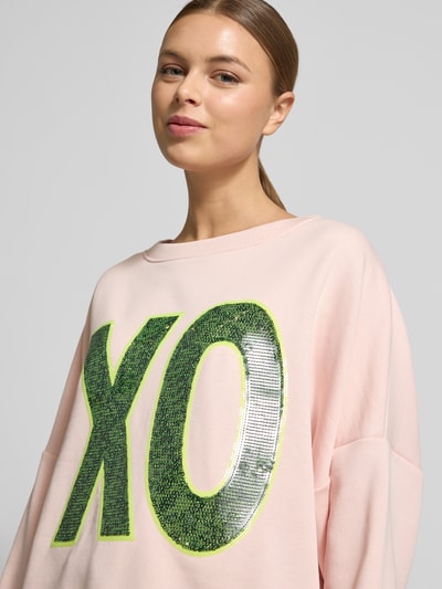 Frauenmodel trägt Oversized Sweatshirt mit Pailettenbesatz Modell 'XO' von miss goodlife in zartem Rosa, Baumwolle, Nahaufnahme Oberkörper.