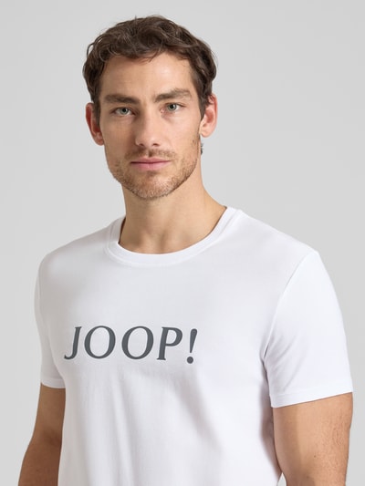 Męski model nosi T-Shirt mit Logo und Rundhalsausschnitt von JOOP! Collection, bawełna z elastanem, krój regular fit, detal logo, biała gładka tkanina, ujęcie: zbliżenie górnej części ciała z przodu.