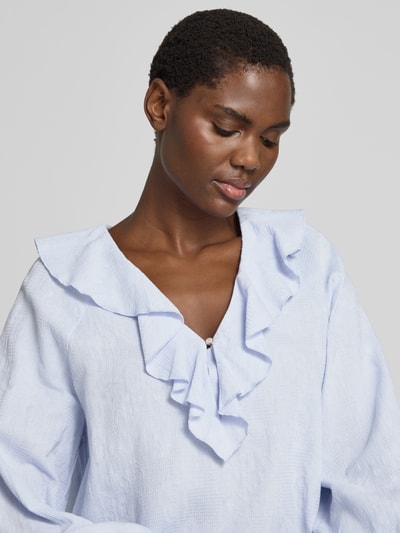 Frauenmodel trägt Regular Fit Bluse mit V-Ausschnitt und Volants von Christian Berg Woman aus feiner, strukturierter Baumwolle in Hellblau, Nahaufnahme Oberkörper.